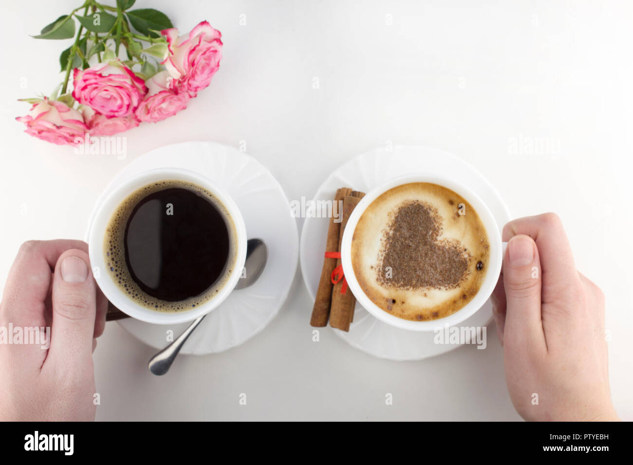 Due tazze di caffè su uno sfondo bianco con le mani, rose Foto Stock