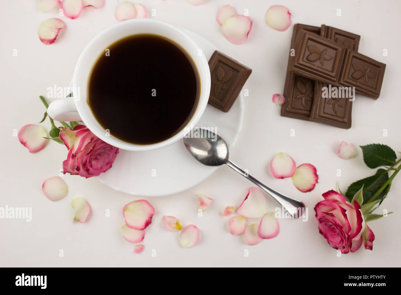 Una tazza di caffè, rose rosse su sfondo bianco e il cioccolato Foto Stock