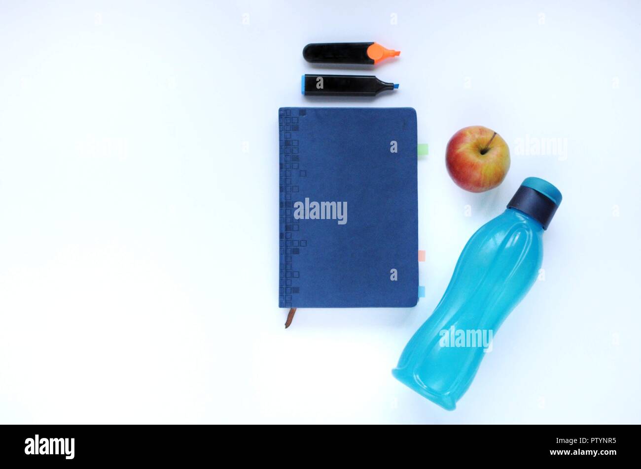 Studio roba. Sfondo dell'istruzione. Articoli di cancelleria. Gli aspetti dell'istruzione. Marcatori, Apple, bottiglia di colore blu e il portatile sul tavolo. Foto Stock