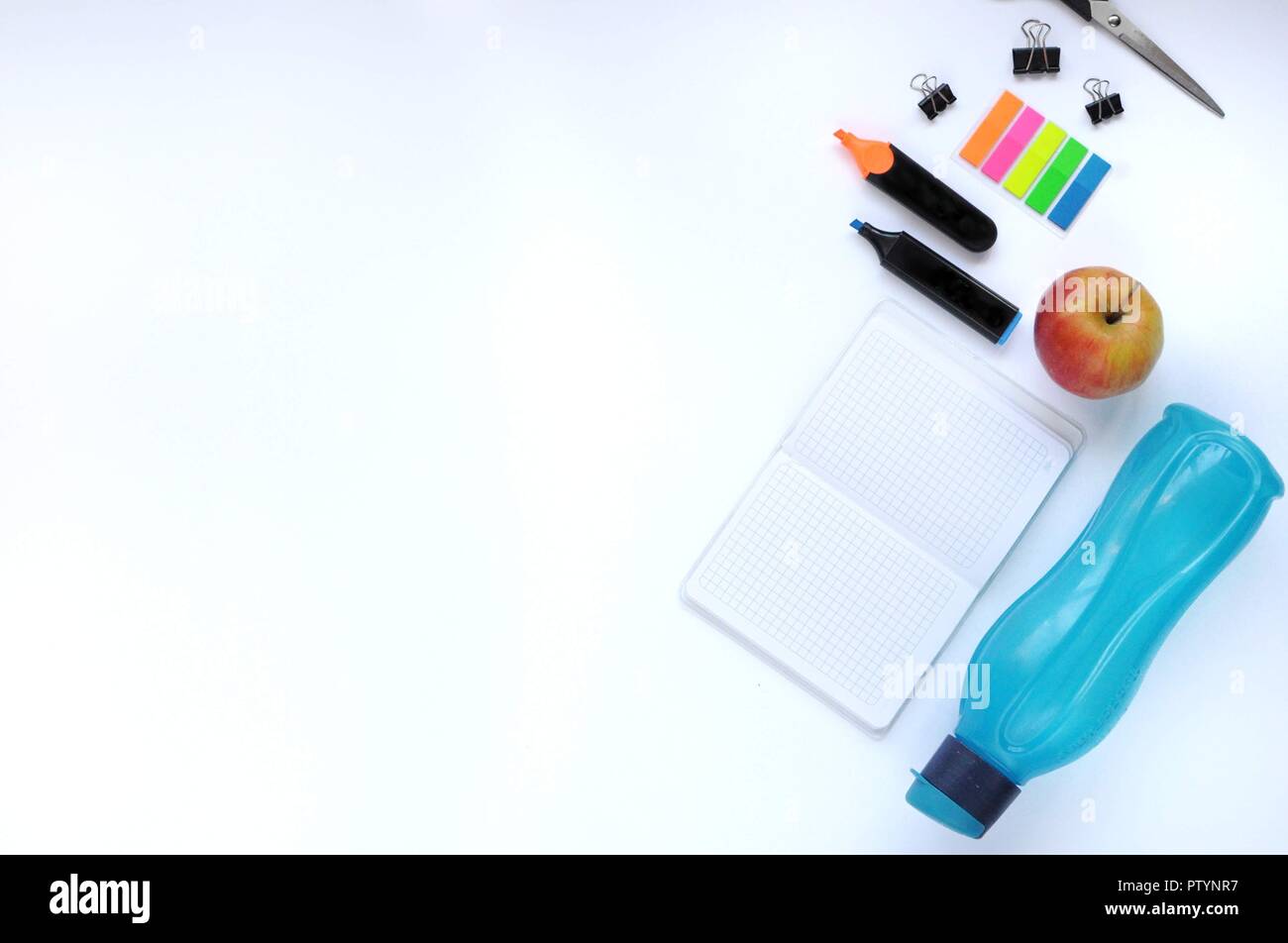 Studio roba. Sfondo dell'istruzione. Articoli di cancelleria. Gli aspetti dell'istruzione. Adesivi, bottiglia, marcatori, forbici, clip, apple e pc portatile sul tavolo. Foto Stock