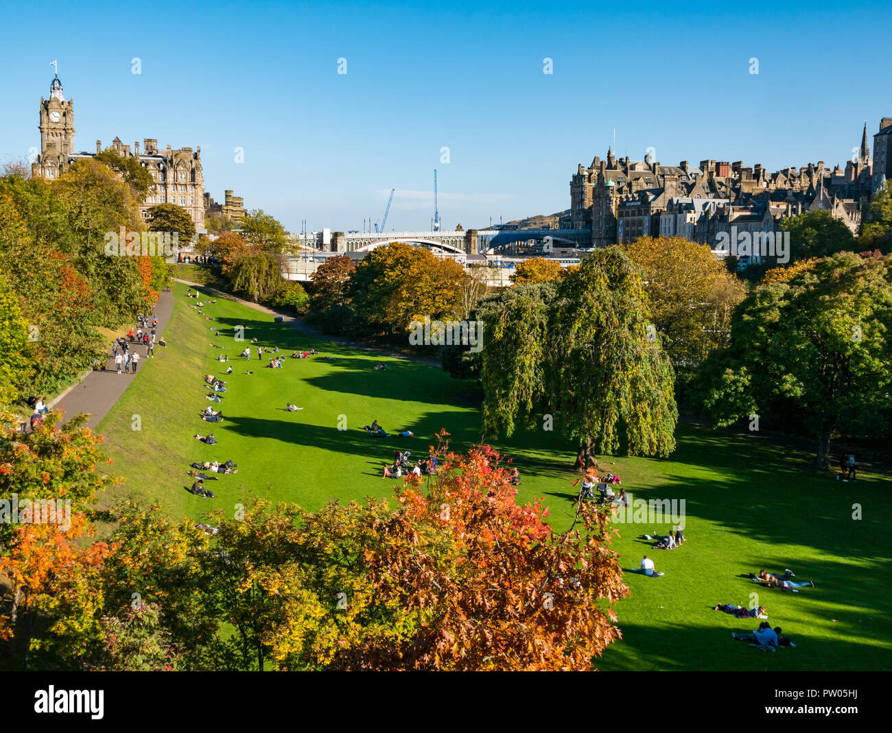 La gente seduta in Princes Street Gardens in sole autunnale con Balmoral Hotel la Torre dell Orologio e North Bridge, Edimburgo, Scozia, Regno Unito Foto Stock