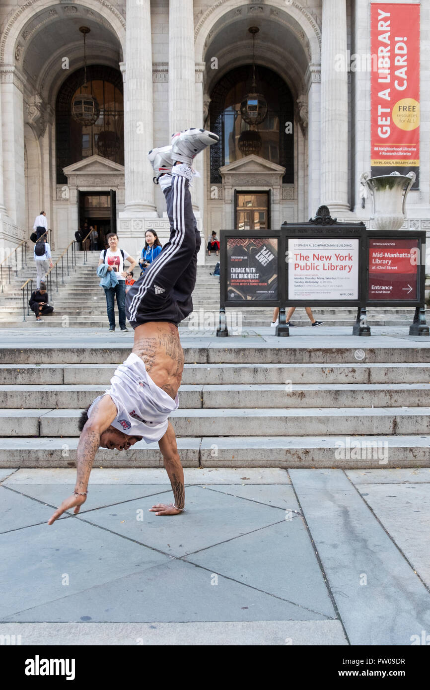 STREET performer. Un acrobatico breakdance busker facendo un handstand nella parte anteriore del ramo principale del New York Public Library sulla Quinta Avenue a Manhattan. Foto Stock