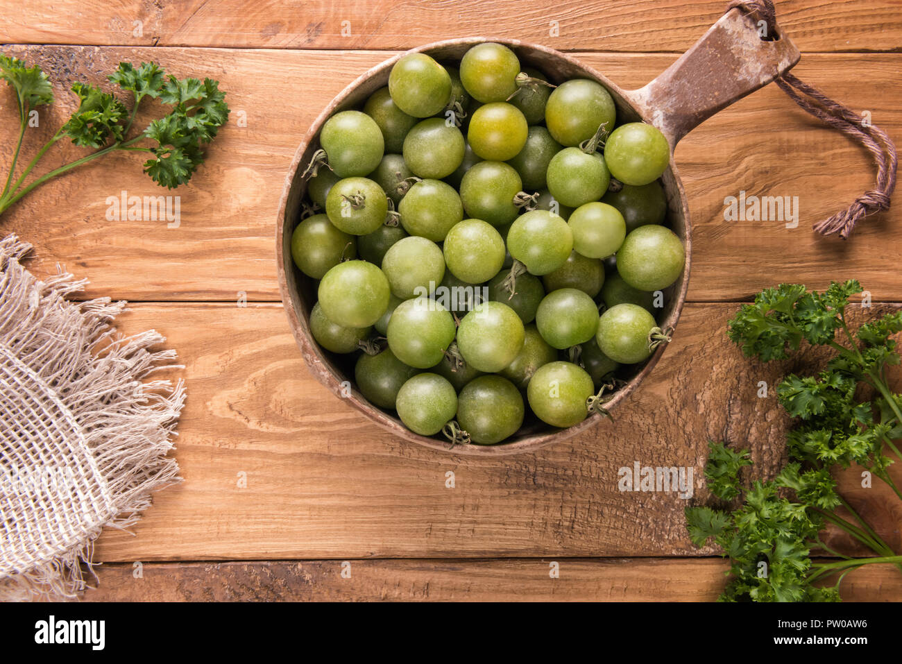 Vista da sopra su verdi maturi delle varietà rotondo piccolo pomodori ciliegia nel ciclo naturale sulla ciotola di legno a trama la superficie del tavolo verde con foglie di prezzemolo Foto Stock