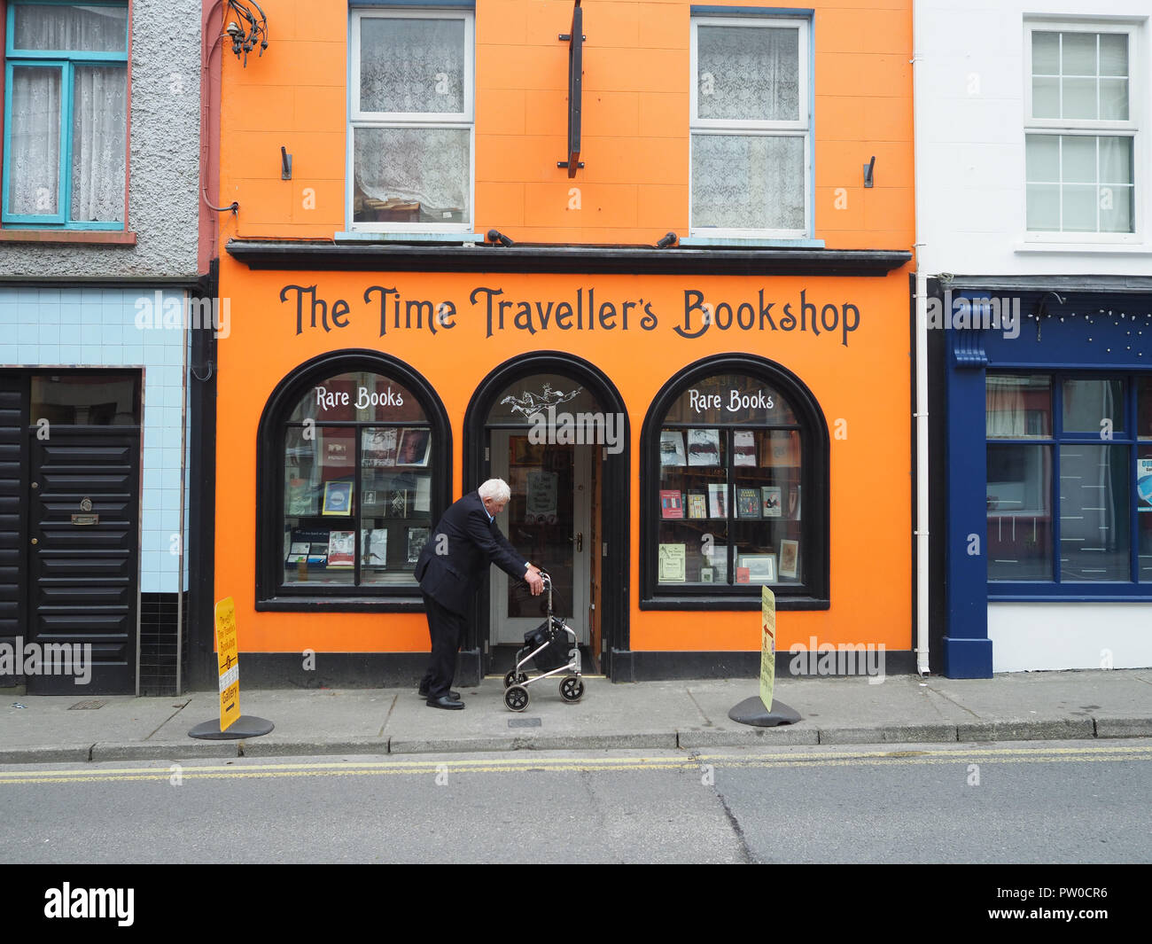 Un vecchio uomo nel profondo del pensiero sul suo telaio zimmer cammina lentamente passato il viaggiatore del tempo libreria in una piccola città sulla costa occidentale dell'Irlanda. Se solo. Foto Stock