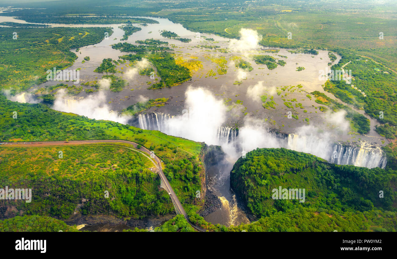 Victoria Falls nello Zimbabwe e Zambia, antenna elicottero foto, foresta verde intorno a incredibili Cascate maestose dell'Africa. Livingston ponte sopra il Foto Stock