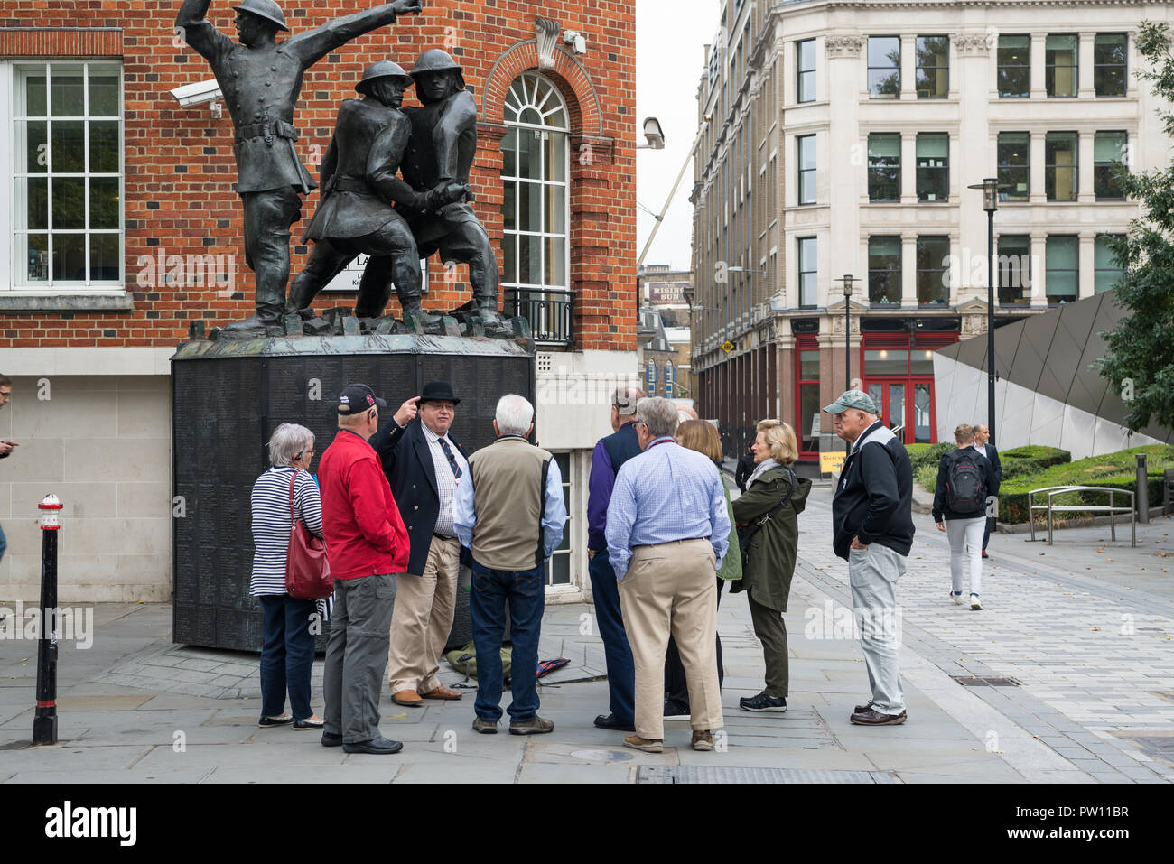 Un tour di Londra guida con un gruppo di turisti americani a livello nazionale vigili del fuoco statua commemorativa nel Carter Lane Gardens, City of London, England, Regno Unito Foto Stock