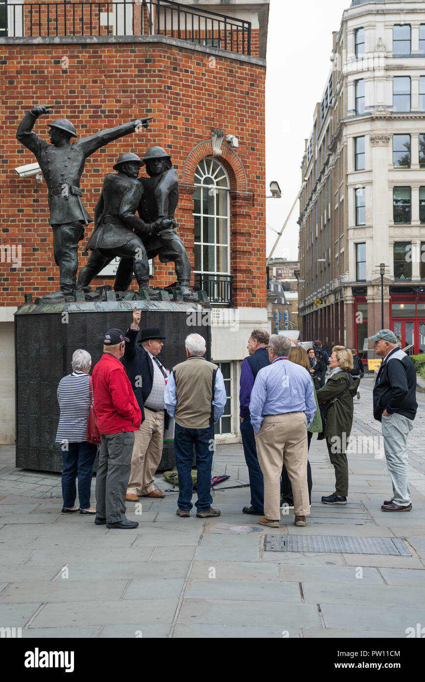 Un tour di Londra guida con un gruppo di turisti americani a livello nazionale vigili del fuoco statua commemorativa nel Carter Lane Gardens, City of London, England, Regno Unito Foto Stock