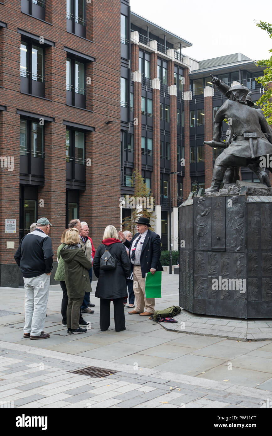 Un tour di Londra guida con un gruppo di turisti americani a livello nazionale vigili del fuoco statua commemorativa nel Carter Lane Gardens, City of London, England, Regno Unito Foto Stock