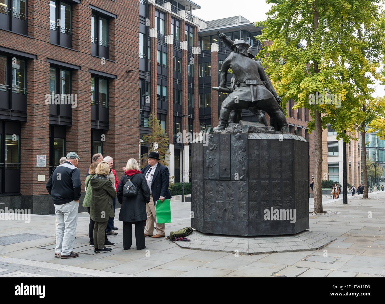 Un tour di Londra guida con un gruppo di turisti americani a livello nazionale vigili del fuoco statua commemorativa nel Carter Lane Gardens, City of London, England, Regno Unito Foto Stock