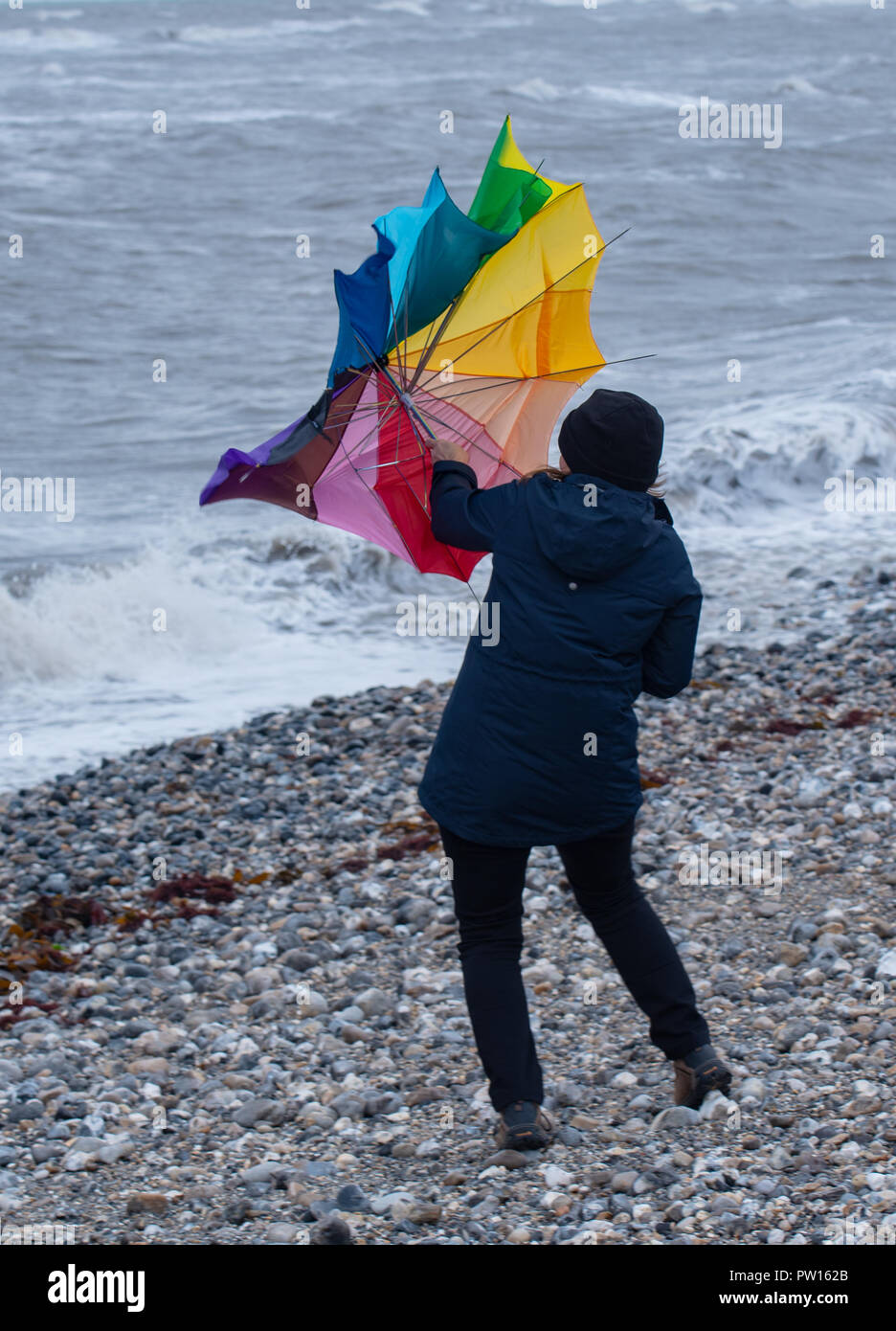 Lyme Regis, Dorset, Regno Unito. 11 ottobre 2018. Regno Unito Meteo: una donna battaglie con un ombrellone sulla spiaggia come gusty venti alti e focolai di pioggia ha colpito il resort costiero di Lyme Regis in anticipo di tempesta Callum. Credito: Celia McMahon/Alamy Live News Foto Stock