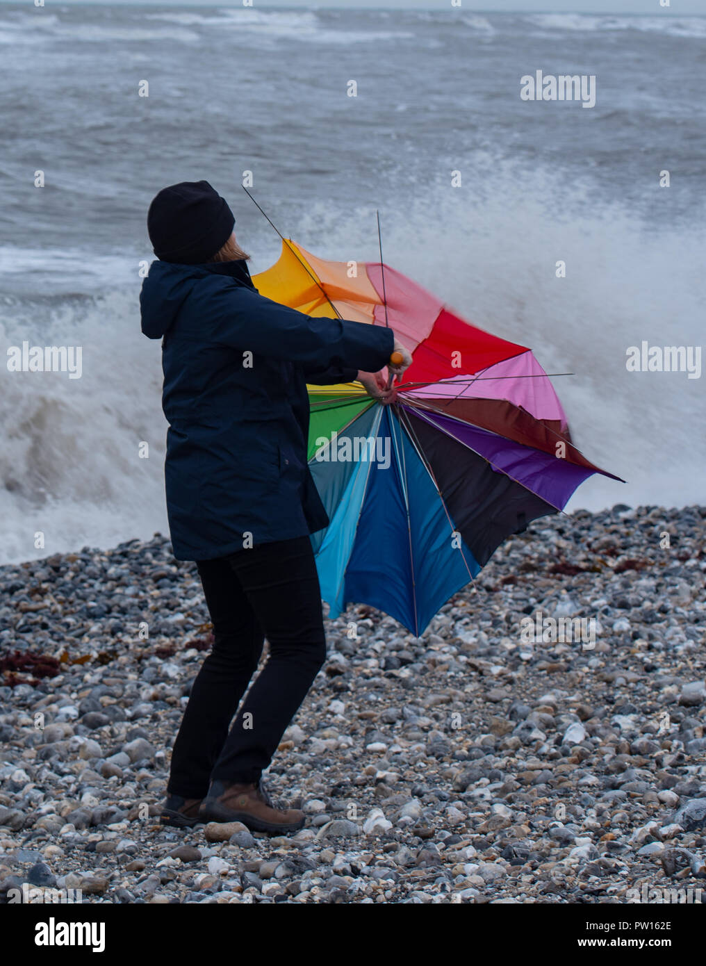 Lyme Regis, Dorset, Regno Unito. 11 ottobre 2018. Regno Unito Meteo: una donna battaglie con un ombrellone sulla spiaggia come gusty venti alti e focolai di pioggia ha colpito il resort costiero di Lyme Regis in anticipo di tempesta Callum. Credito: Celia McMahon/Alamy Live News Foto Stock