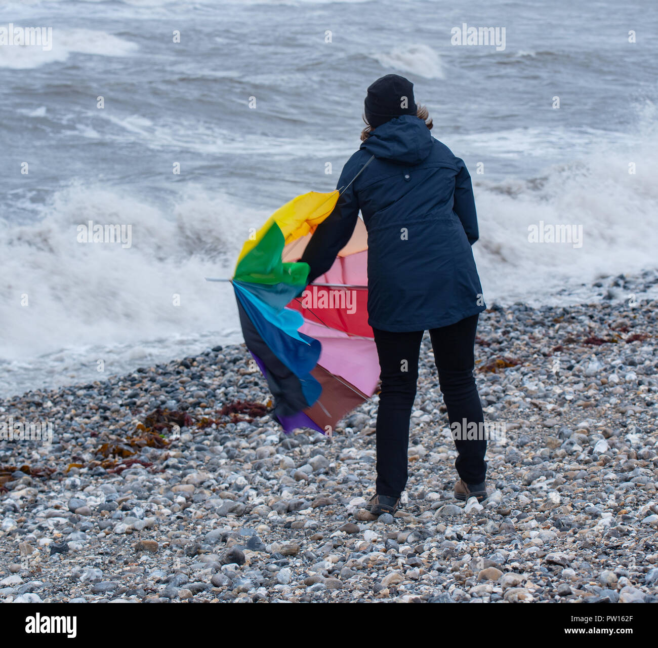 Lyme Regis, Dorset, Regno Unito. 11 ottobre 2018. Regno Unito Meteo: una donna battaglie con un ombrellone sulla spiaggia come gusty venti alti e focolai di pioggia ha colpito il resort costiero di Lyme Regis in anticipo di tempesta Callum. Credito: Celia McMahon/Alamy Live News Foto Stock