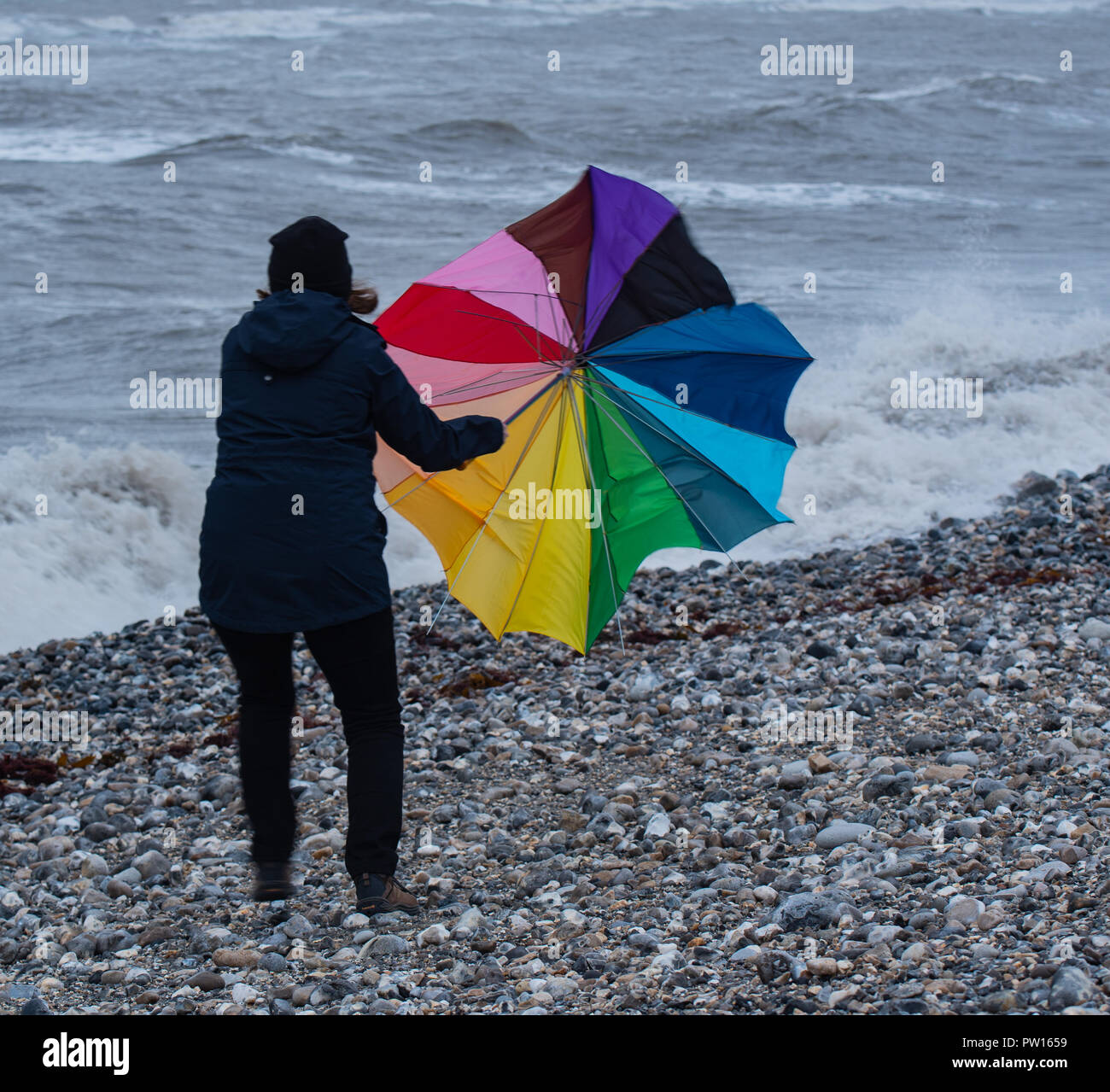 Lyme Regis, Dorset, Regno Unito. 11 ottobre 2018. Regno Unito Meteo: una donna battaglie con un ombrellone sulla spiaggia come gusty venti alti e focolai di pioggia ha colpito il resort costiero di Lyme Regis in anticipo di tempesta Callum. Credito: Celia McMahon/Alamy Live News Foto Stock