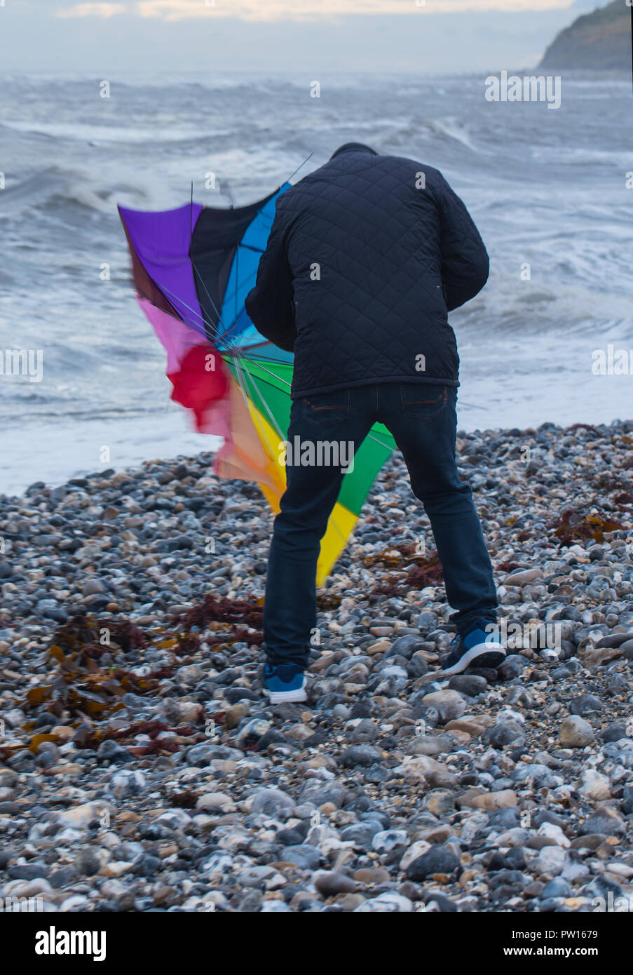 Lyme Regis, Dorset, Regno Unito. 11 ottobre 2018. Regno Unito Meteo: un uomo di battaglie con un ombrellone sulla spiaggia come gusty venti alti e focolai di pioggia ha colpito il resort costiero di Lyme Regis in anticipo di tempesta Callum. Credito: Celia McMahon/Alamy Live News Foto Stock