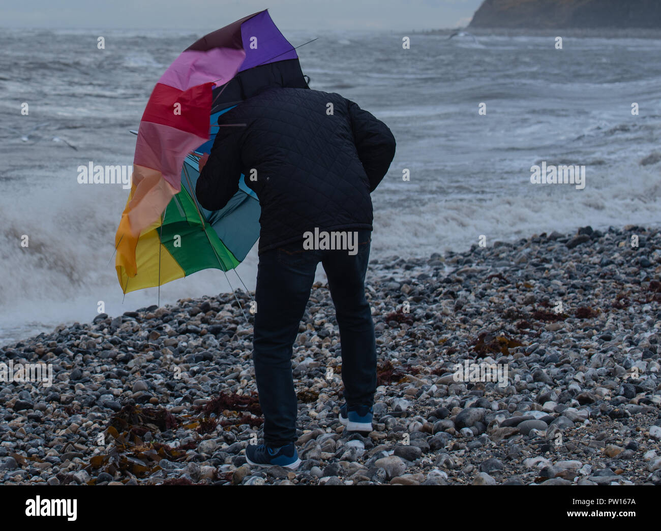 Lyme Regis, Dorset, Regno Unito. 11 ottobre 2018. Regno Unito Meteo: un uomo di battaglie con un ombrellone sulla spiaggia come gusty venti alti e focolai di pioggia ha colpito il resort costiero di Lyme Regis in anticipo di tempesta Callum. Credito: Celia McMahon/Alamy Live News Foto Stock