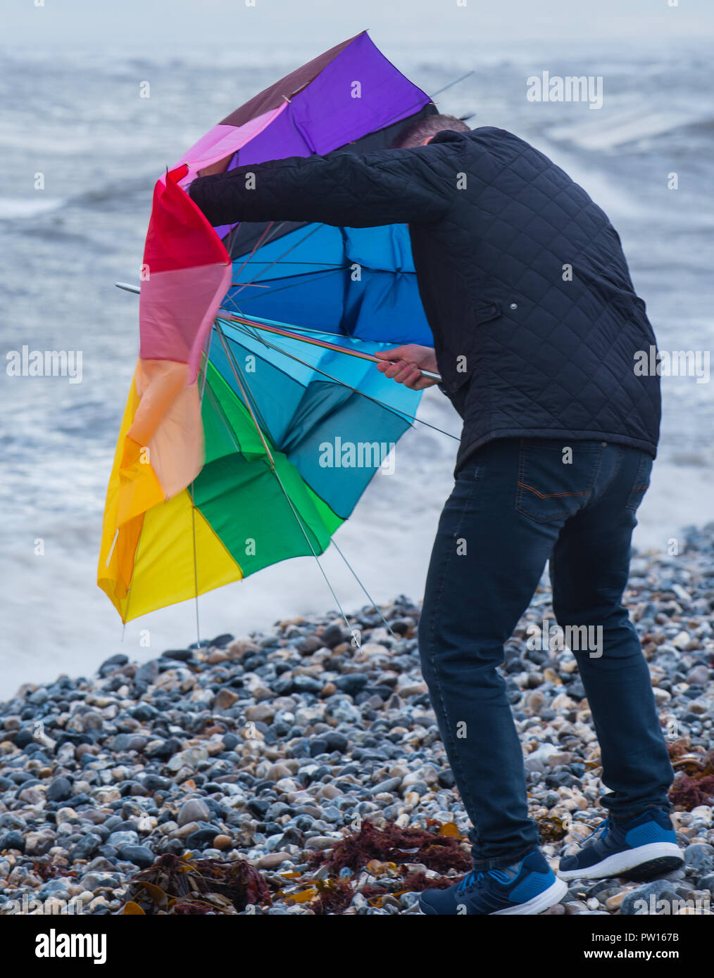 Lyme Regis, Dorset, Regno Unito. 11 ottobre 2018. Regno Unito Meteo: un uomo di battaglie con un ombrellone sulla spiaggia come gusty venti alti e focolai di pioggia ha colpito il resort costiero di Lyme Regis in anticipo di tempesta Callum. Credito: Celia McMahon/Alamy Live News Foto Stock