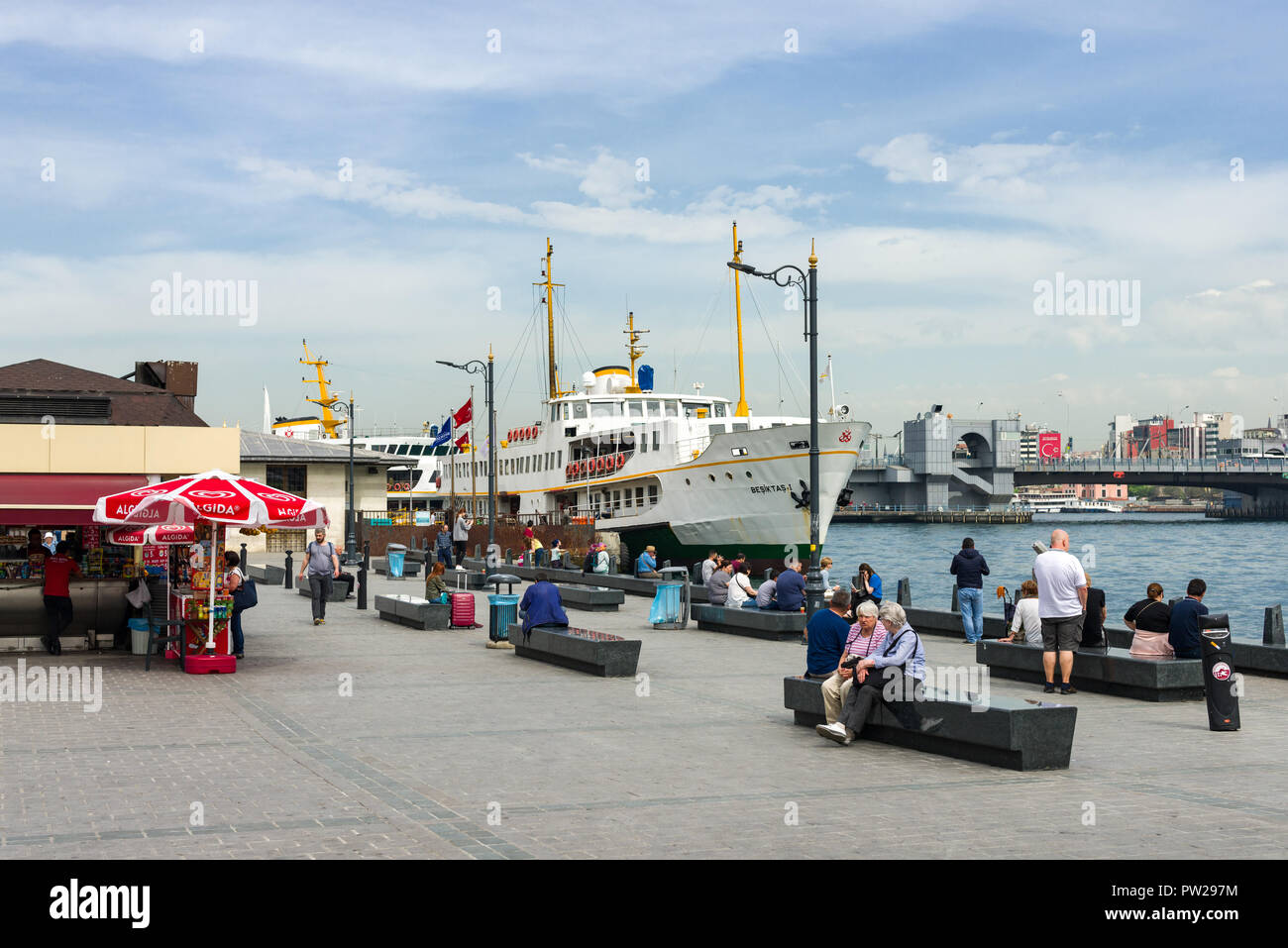 La gente seduta su sedili di pietra dal molo Eminonu con traghetto attraccato in background, Istanbul, Turchia Foto Stock