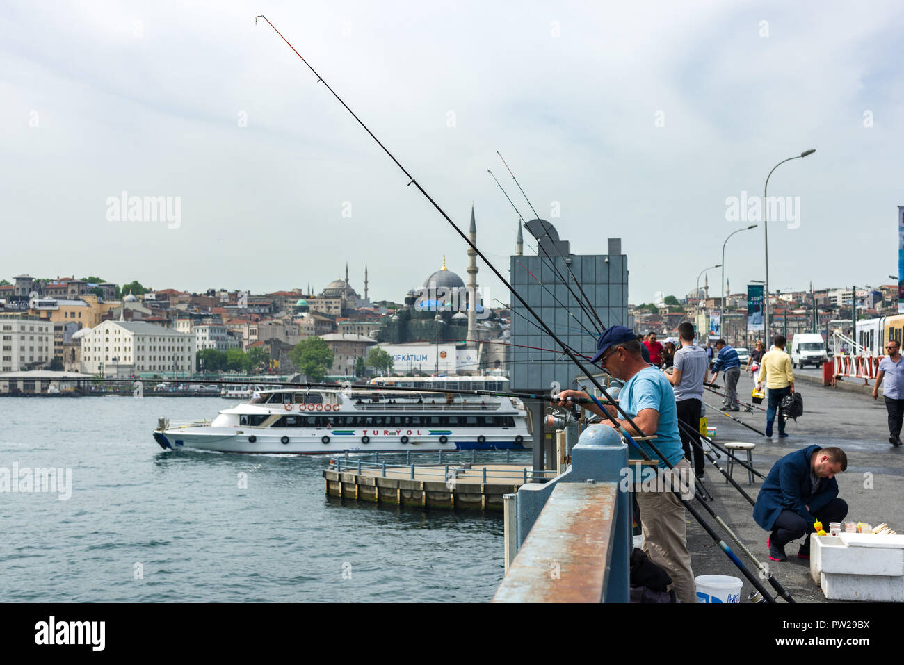 Un gruppo di pescatori di sostare sul Ponte di Galata con le loro canne da pesca oltre il lato come un traghetto passa da, Istanbul, Turchia Foto Stock