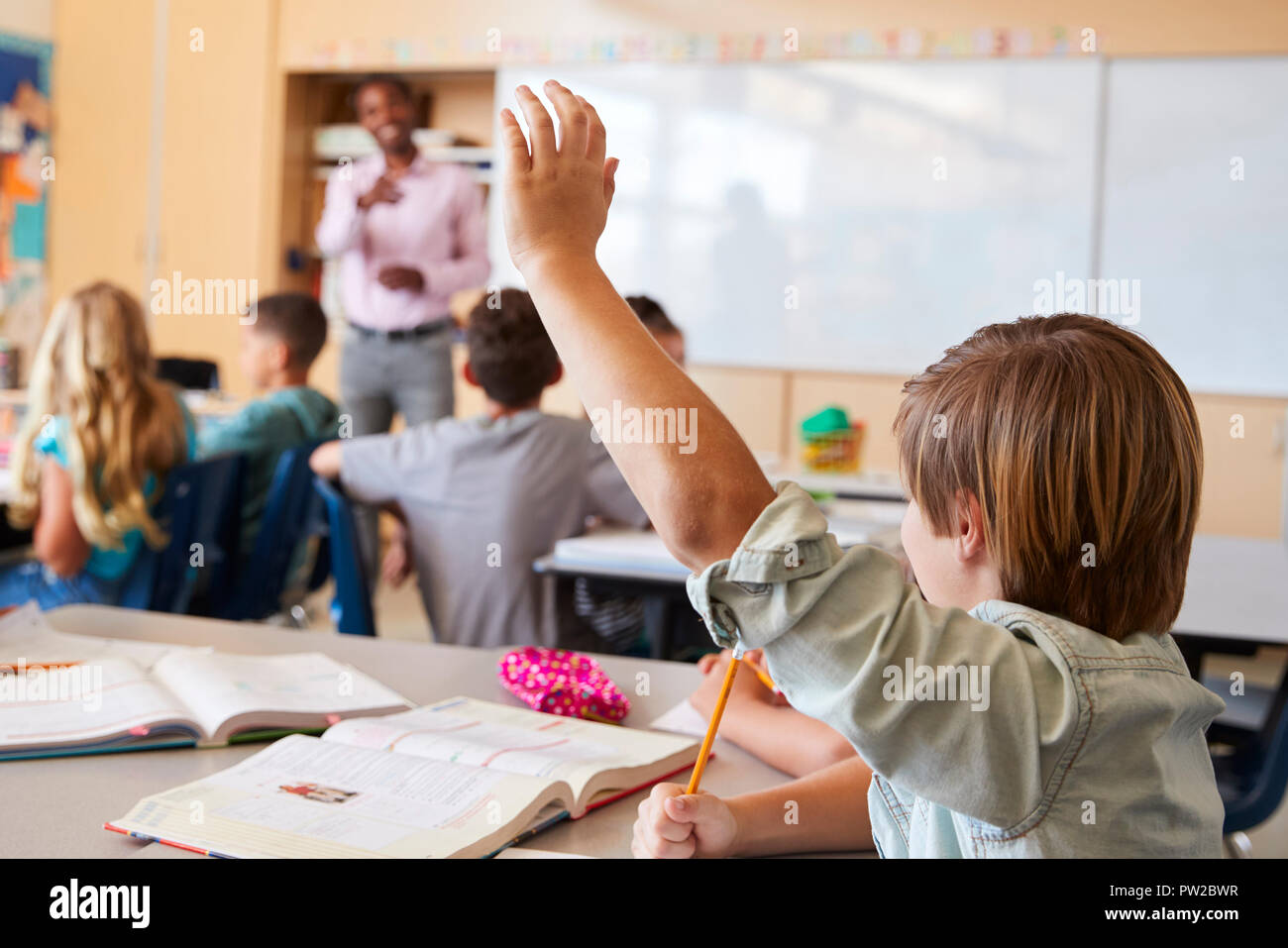 Scolaro alzando la mano per rispondere alla domanda in una classe della scuola Foto Stock