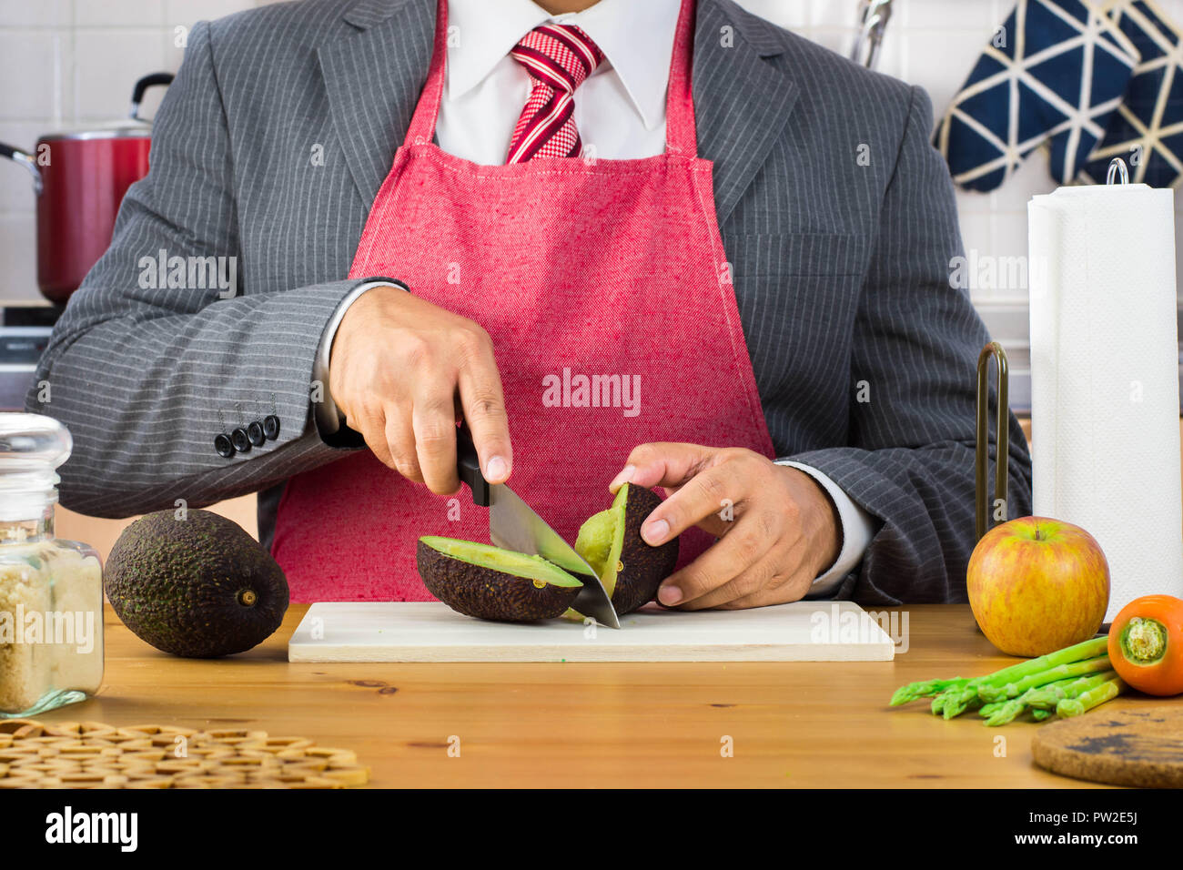 Un imprenditore, Padre, il marito e la cravatta rossa che indossa il grembiule e tenendo un piccolo pelato banana in cucina. Foto Stock