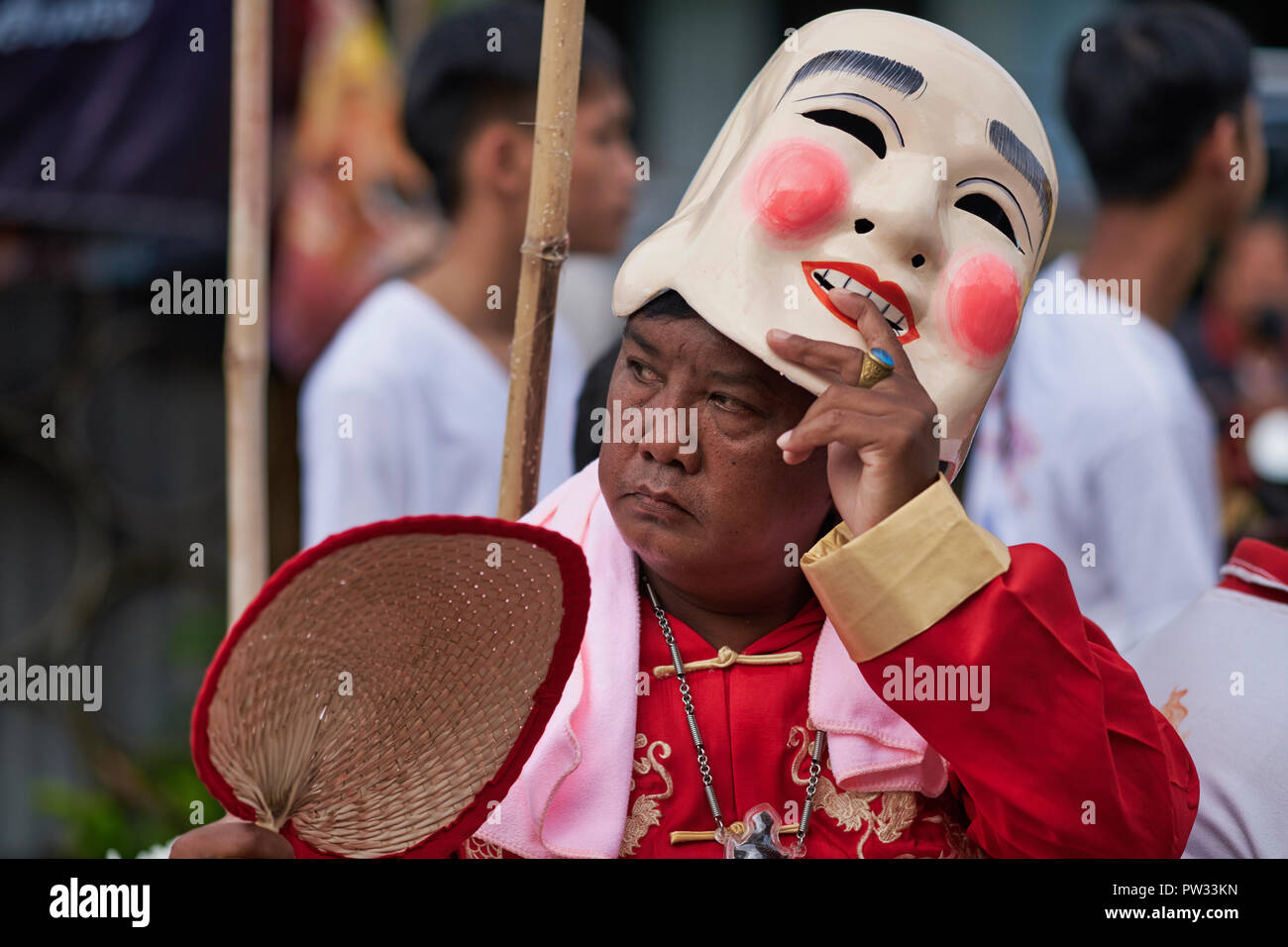 Una processione durante il Festival vegetariano di Phuket, in Thailandia, con un uomo che solleva la sua maschera cinese sorridente per rivelare il suo volto cupo sotto Foto Stock