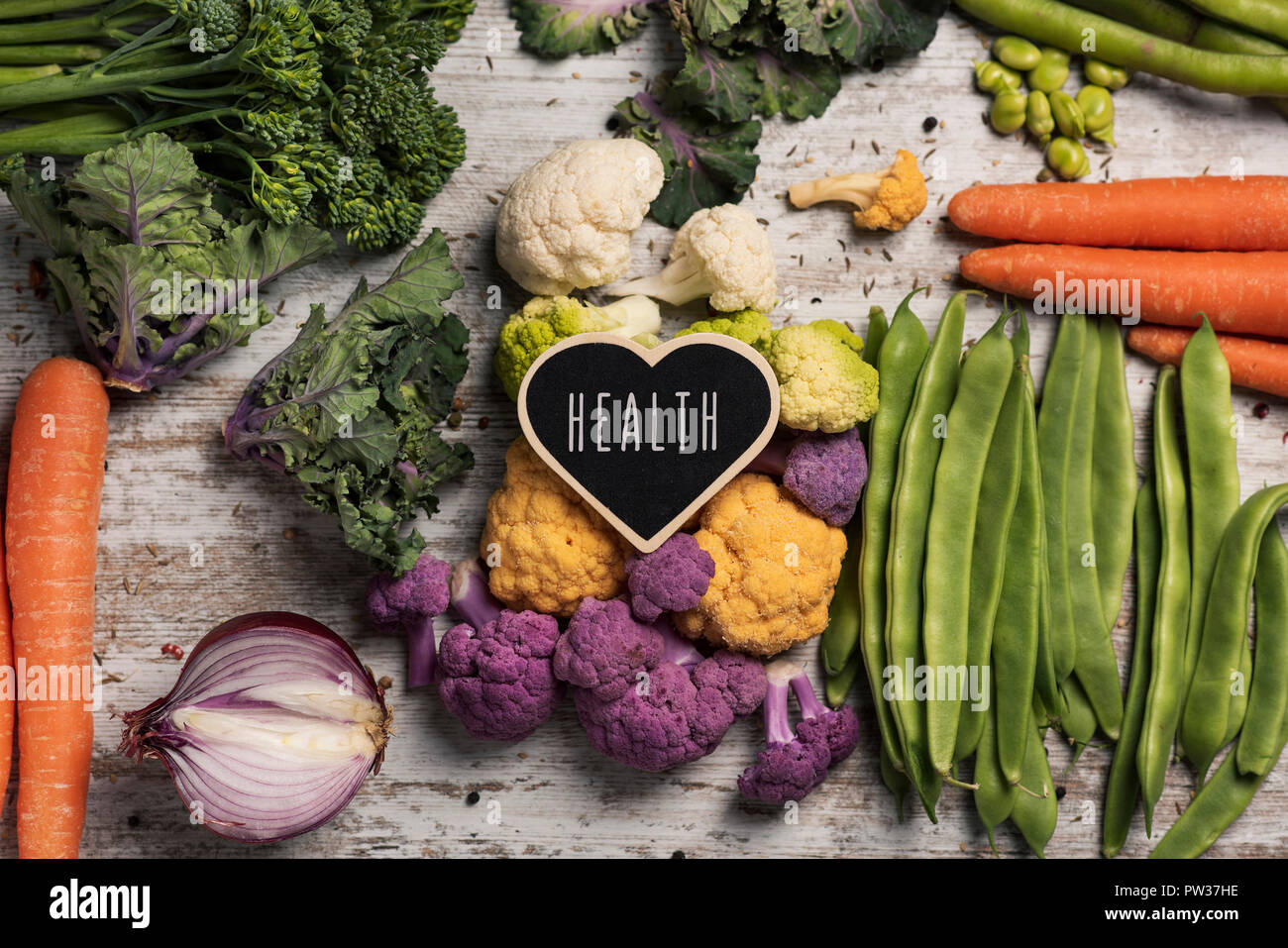 A heart-shaped cartello con la salute del testo scritto in esso, disposto su una pila di alcune diverse verdure crude, come ad esempio il cavolfiore, broccolini, fava Foto Stock