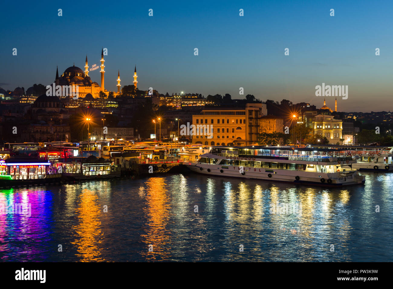 La luminosa cucina galleggiante di barche di Eminonu con la moschea di Suleymaniye e Golden Horn in background al crepuscolo, Istanbul, Turchia Foto Stock