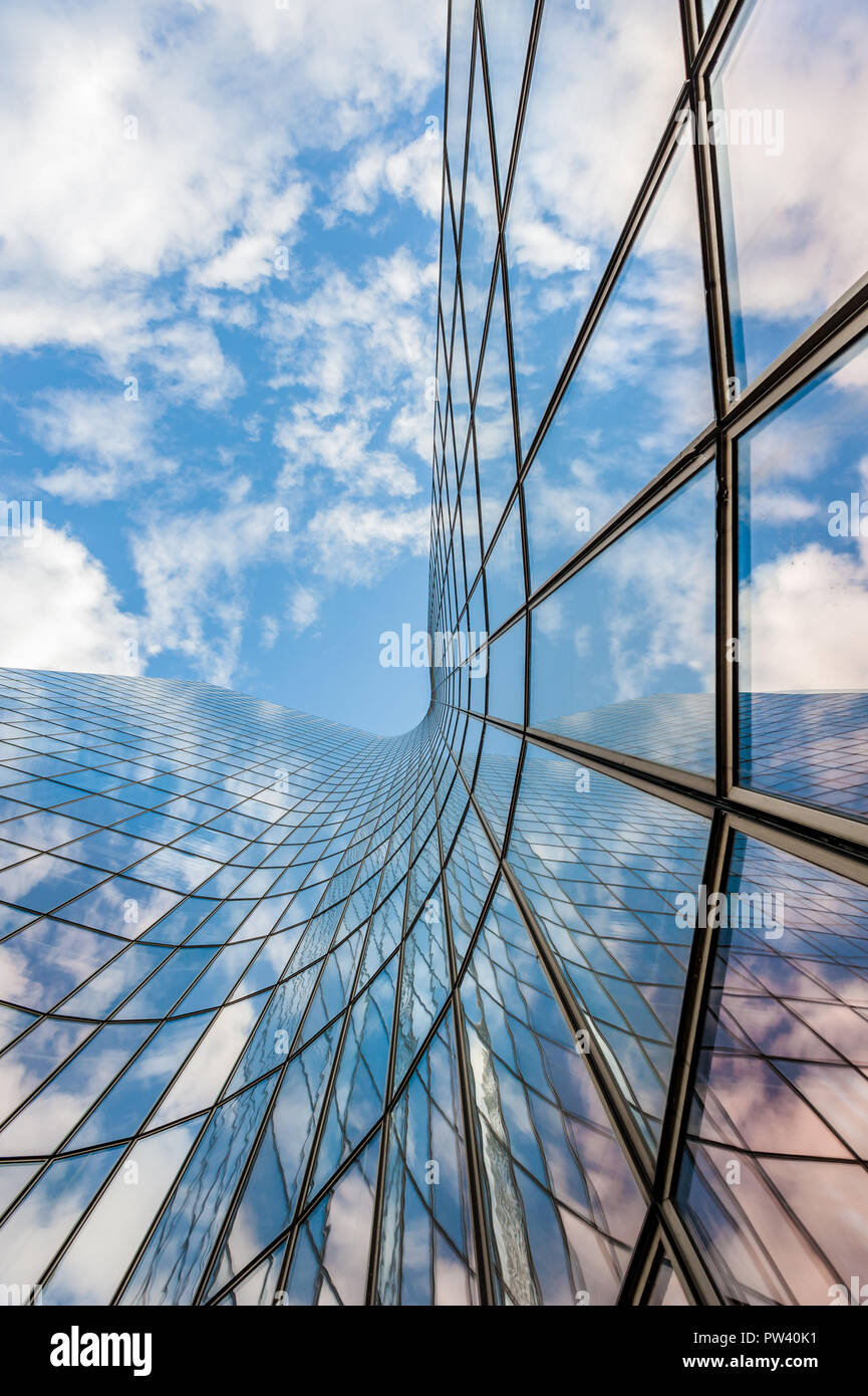 Vetro edificio curvo che riflette il cielo blu e nuvole bianche a basso angolo di visione Foto Stock