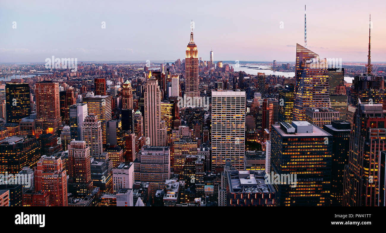 Una vista panoramica di Manhattan, New York, NY, gli Stati Uniti. Una piacevole armonia di luci gialle della città e il tramonto rossastro che si riflette sugli edifici degli uffici. Foto Stock