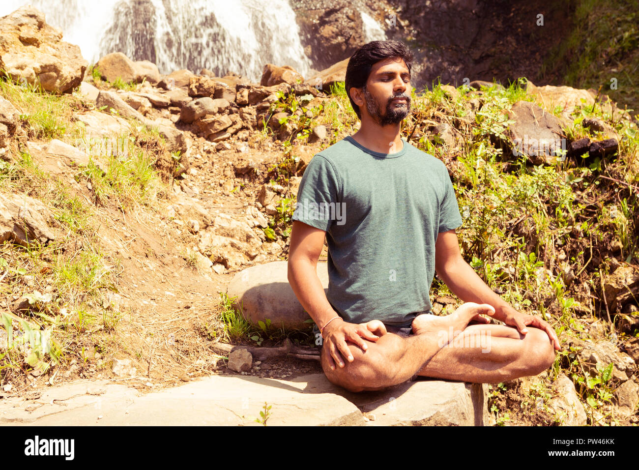 Maschio indiano maestro di Yoga meditazione chiudendo gli occhi su pietre in seduta lotus posano con sfondo naturale Foto Stock