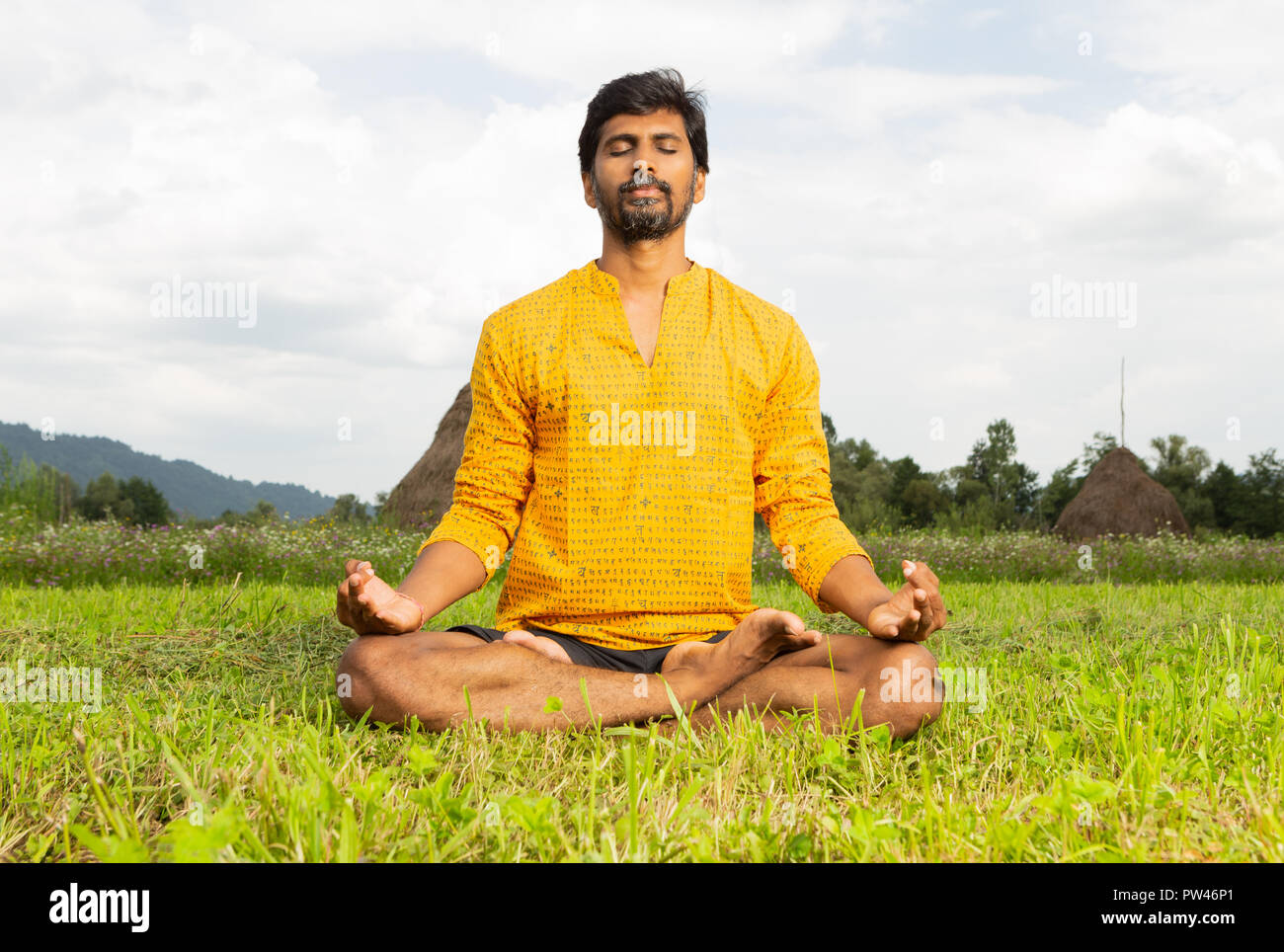 Uomo indiano yogi in lotus pongono in appoggio le mani sulle ginocchia in seduta erba come sfondo naturale Foto Stock