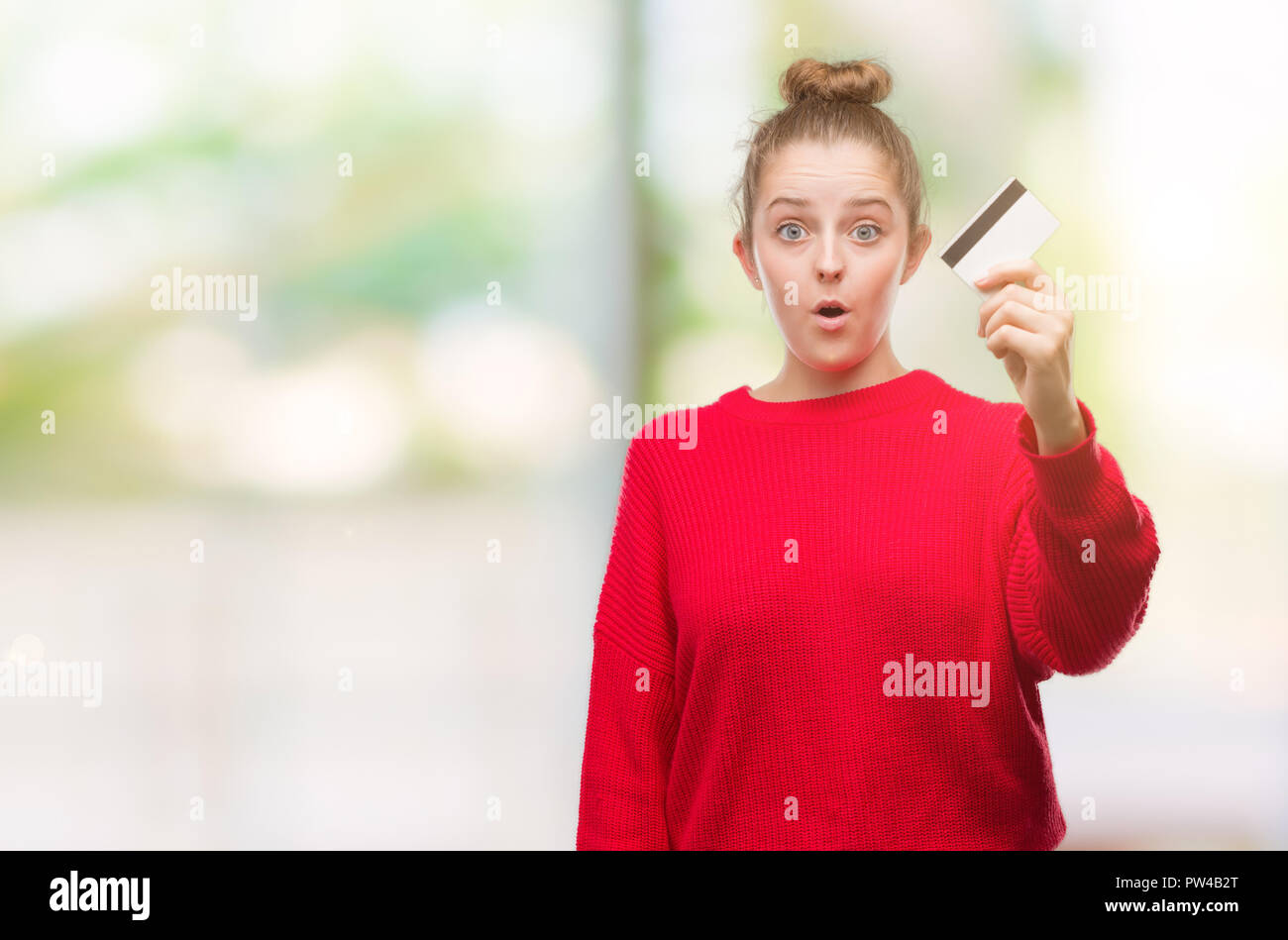 Giovane donna bionda azienda carta di credito paura in stato di shock con una faccia a sorpresa, paura e eccitati con espressione di paura Foto Stock