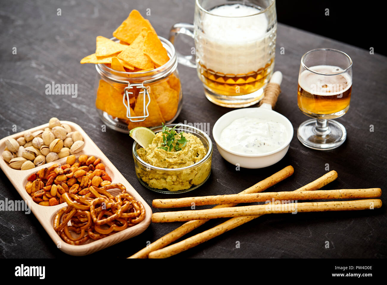 Birra e una ciotola di guacamole con nachos e snack salati su un vecchio nero tavolo di legno in un pub Foto Stock