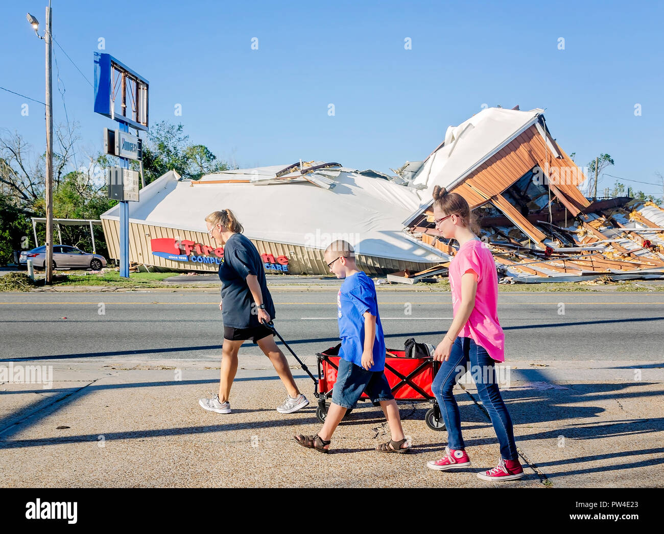 Danielle Merchant tira un carro come lei e i suoi figli a piedi passato gli edifici danneggiati nella città di Panama, in Florida dopo l uragano Michael. Foto Stock
