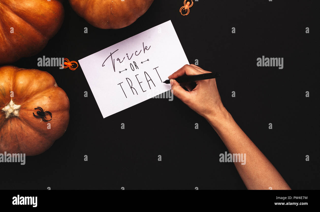 Zucche e ragni su sfondo nero con mani femminili iscritto dolcetto o scherzetto su una scheda. Tema di Halloween lay piatto su sfondo nero. Foto Stock