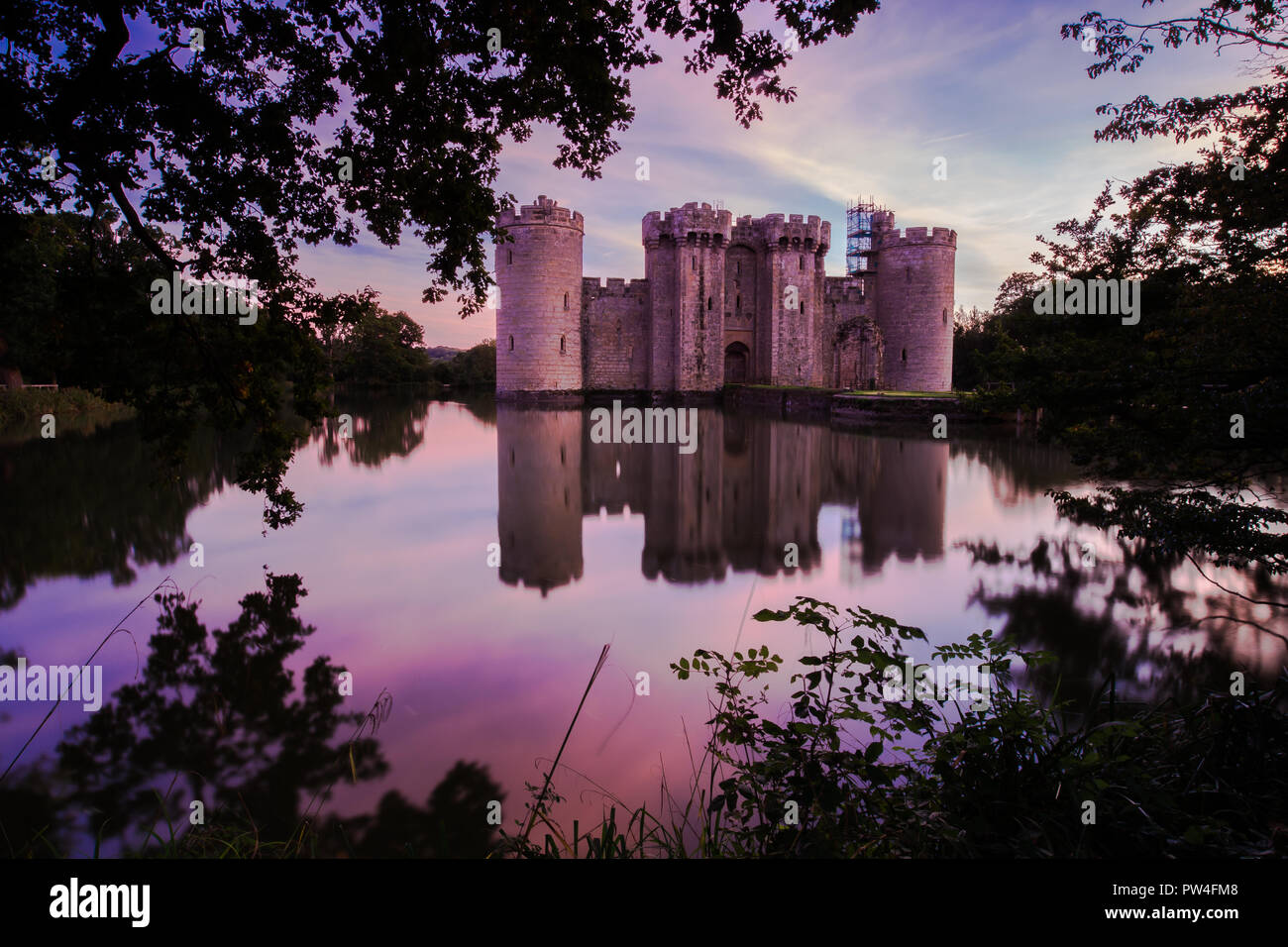 Il Castello di Bodiam, East Sussex, al tramonto con il tramonto del sole e cielo lilla con riflessi nel fossato Foto Stock