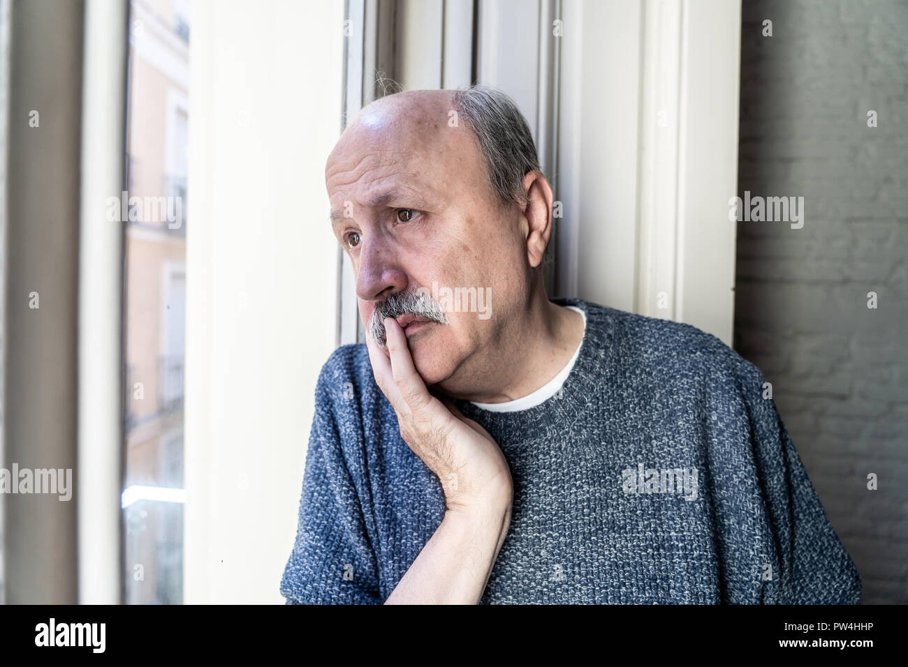 Il vecchio uomo senior cercando in tutta la finestra sentirsi confuso e depresso da soli a casa in invecchiamento pensione di vedovo la demenza di Alzheimer e concetto. Foto Stock