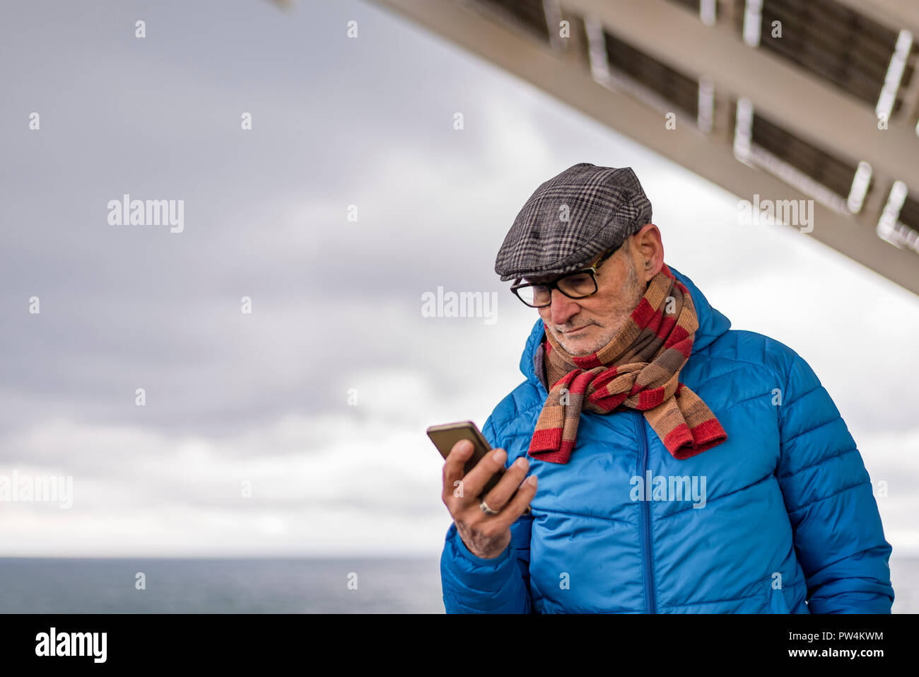 Senior uomo utilizzando smart phone mentre in piedi dal mare contro il cielo nuvoloso Foto Stock