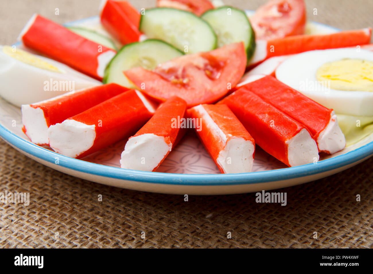 Bastoncini di granchio, uovo sodo e appena fette di pomodoro e cetriolo sul piatto di portata in ceramica bianca Foto Stock