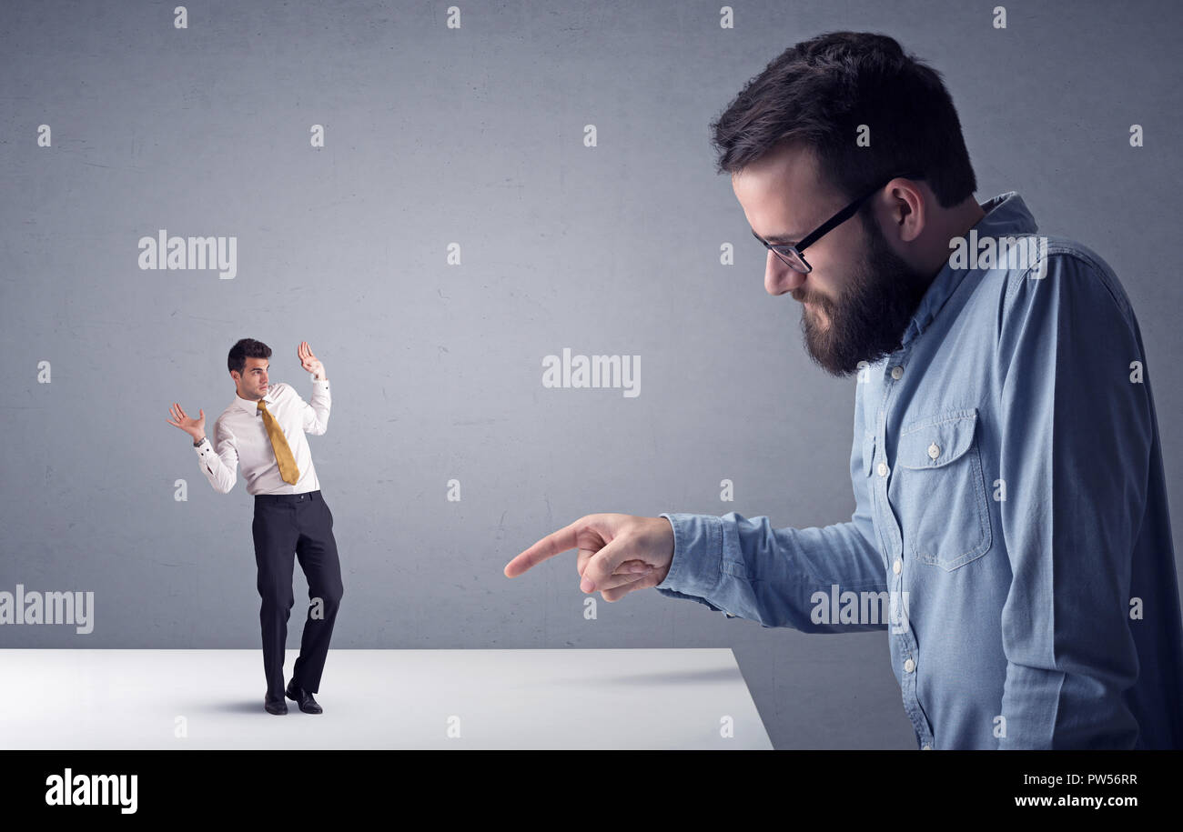 Giovane imprenditore professionale essendo arrabbiato con un altro imprenditore in miniatura di fronte a uno sfondo grigio Foto Stock