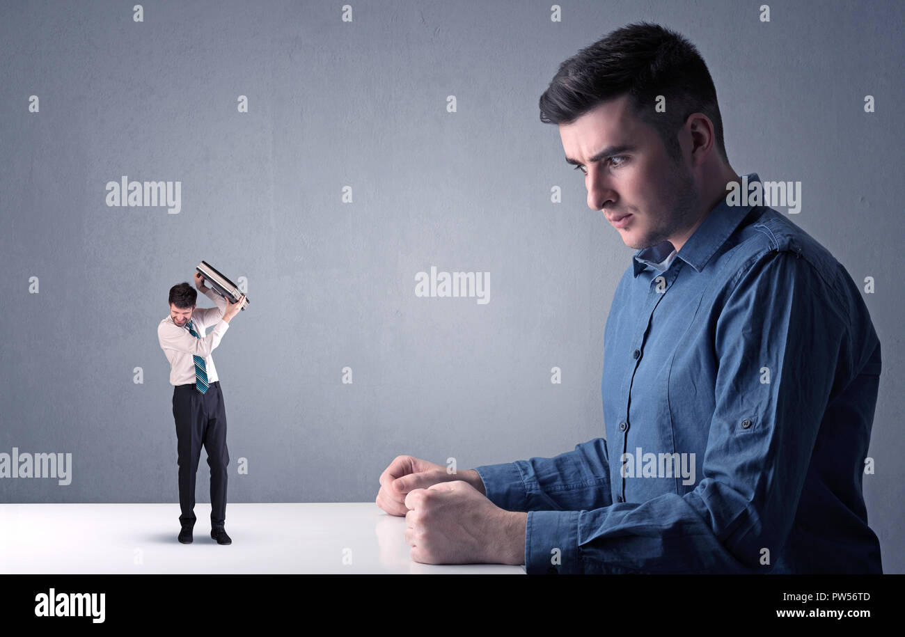 Giovane imprenditore professionale essendo arrabbiato con un altro imprenditore in miniatura nella parte anteriore di un bluastro sfondo grigio Foto Stock