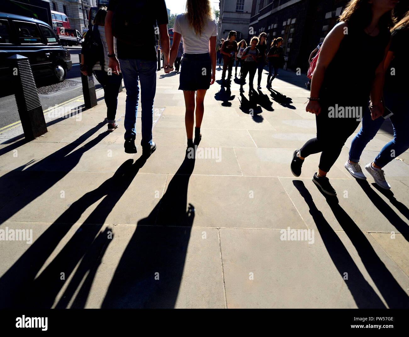 Coppia giovane camminando mano nella mano in Whitehall, Londra, Inghilterra, Regno Unito. Retroilluminati Foto Stock