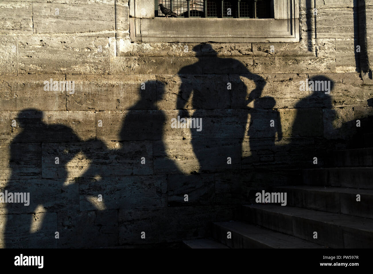 Le ombre delle persone in un vero e proprio muro di pietra in corrispondenza della nuova moschea a Istanbul. Alcune persone sono seduti e passeggiate e un padre è tenendo la sua mano per bambini. Foto Stock