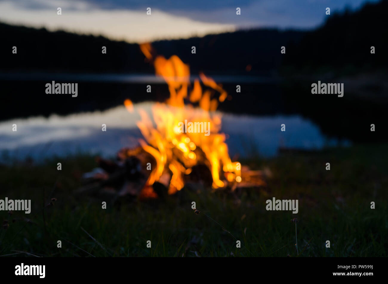 Campfire dopo il tramonto in montagna accanto a un lago Foto Stock