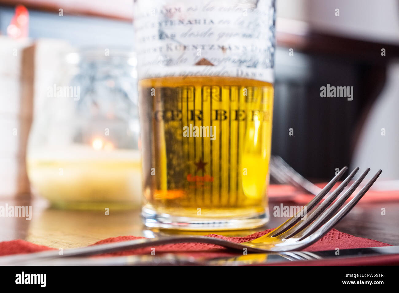 Mezza bevuto un bicchiere di birra lager e una forcella su un tavolo in un bar Foto Stock