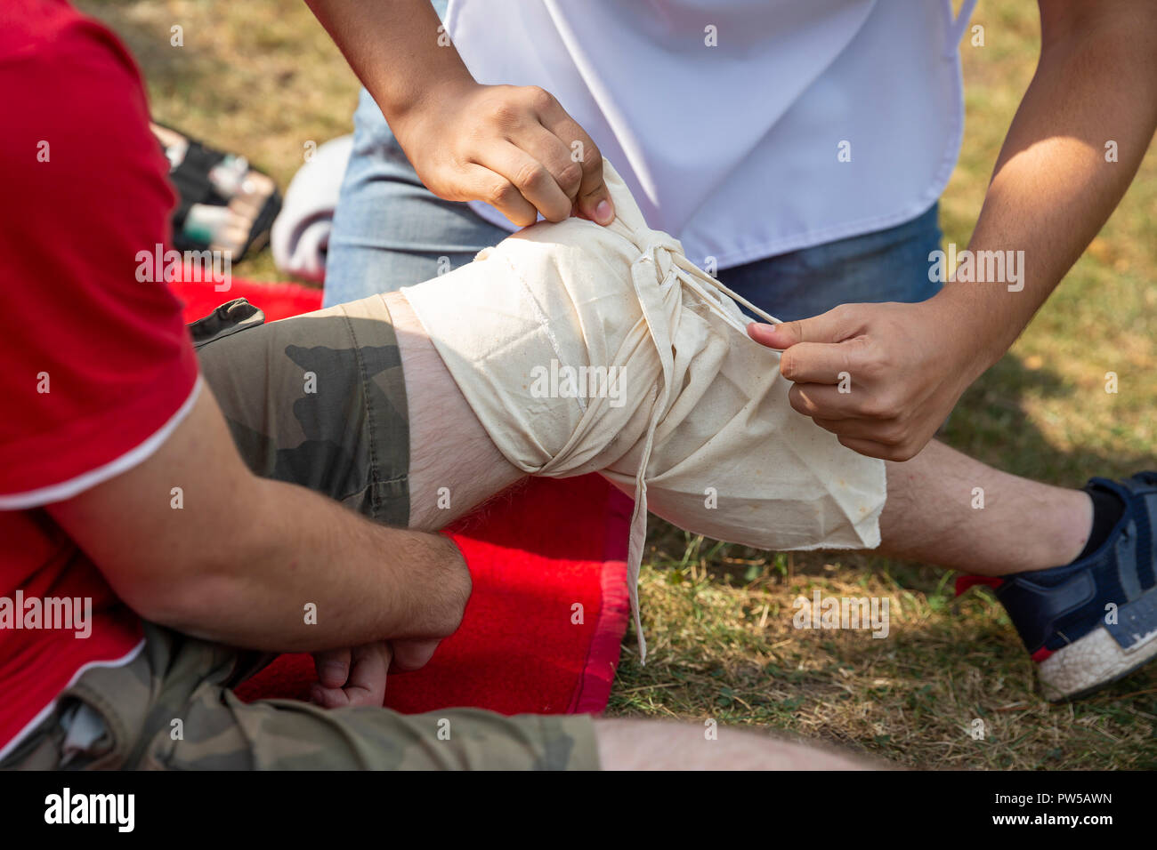 Paziente avente la sua gamba bendata sul terreno da un volontario. Foto Stock