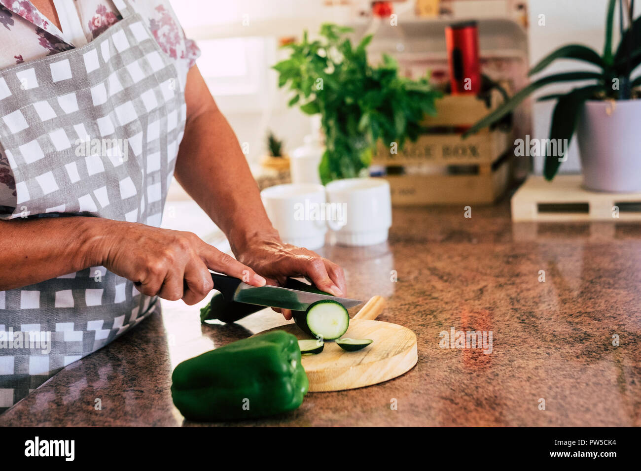 Close up di età donna matura mani il taglio e la cottura di verdura per un sano pranzo o cena a casa, cucina scena quotidiana con la nonna lavora Foto Stock