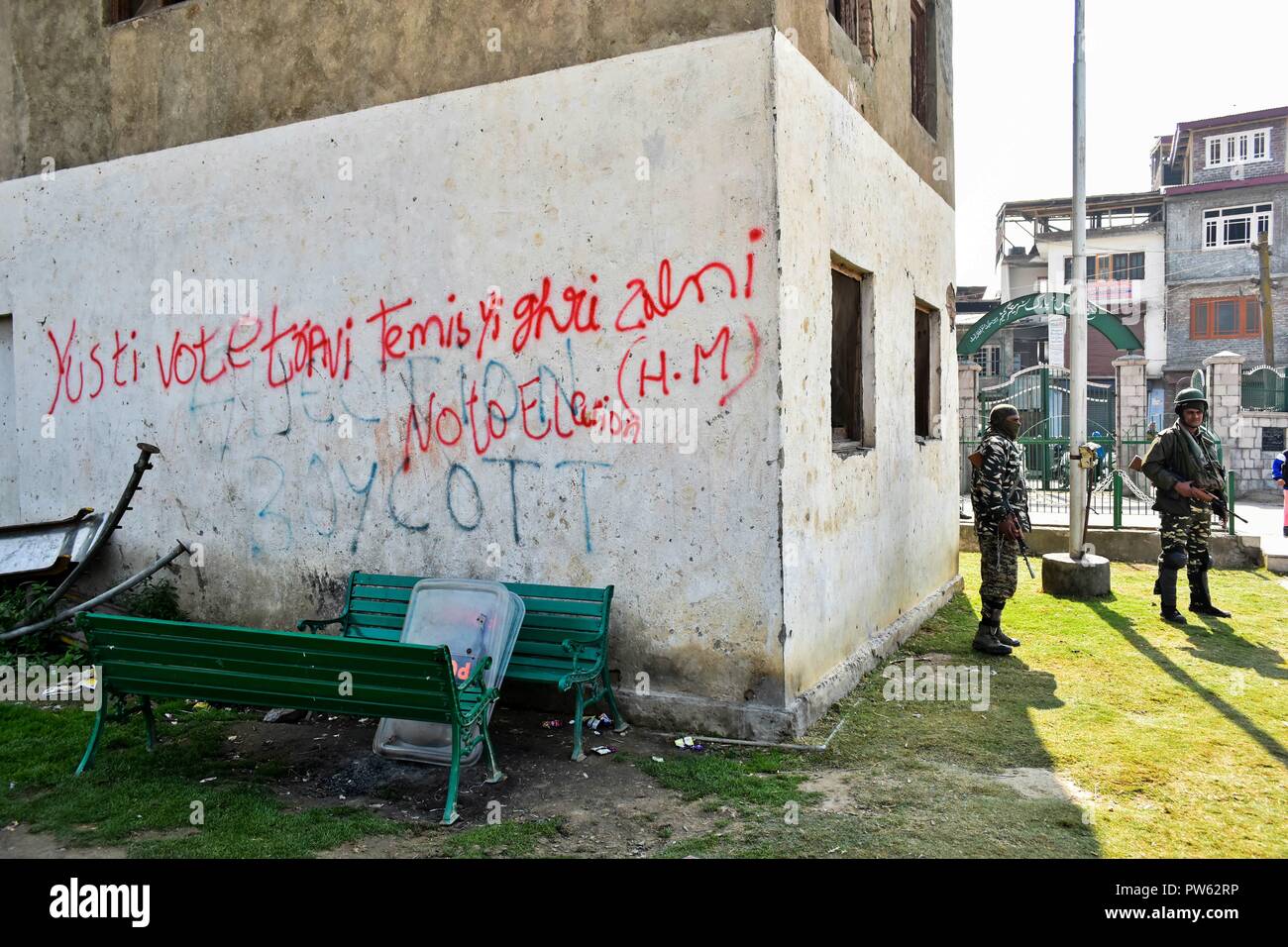 Srinagar Kashmir. 13 ottobre 2018. Di paramilitari troopers guardia accanto a una parete con anti-graffiti elettorale all'interno della stazione di polling durante la terza fase delle elezioni locali in SrinagarKashmir. La terza fase del Jammu e Kashmir urbano corpo locale elezioni ha cominciato attraverso 300 seggi alle 6 di mattina del sabato in mezzo alle severe misure di sicurezza. Come molti come 365 candidati sono in mischia per le elezioni. Una spessa coltre di sicurezza è stata gettata intorno ai seggi, mentre le forze di sicurezza stanno conducendo dominazione area di esercizi per garantire un incidente-libera elezione, funzionari Foto Stock