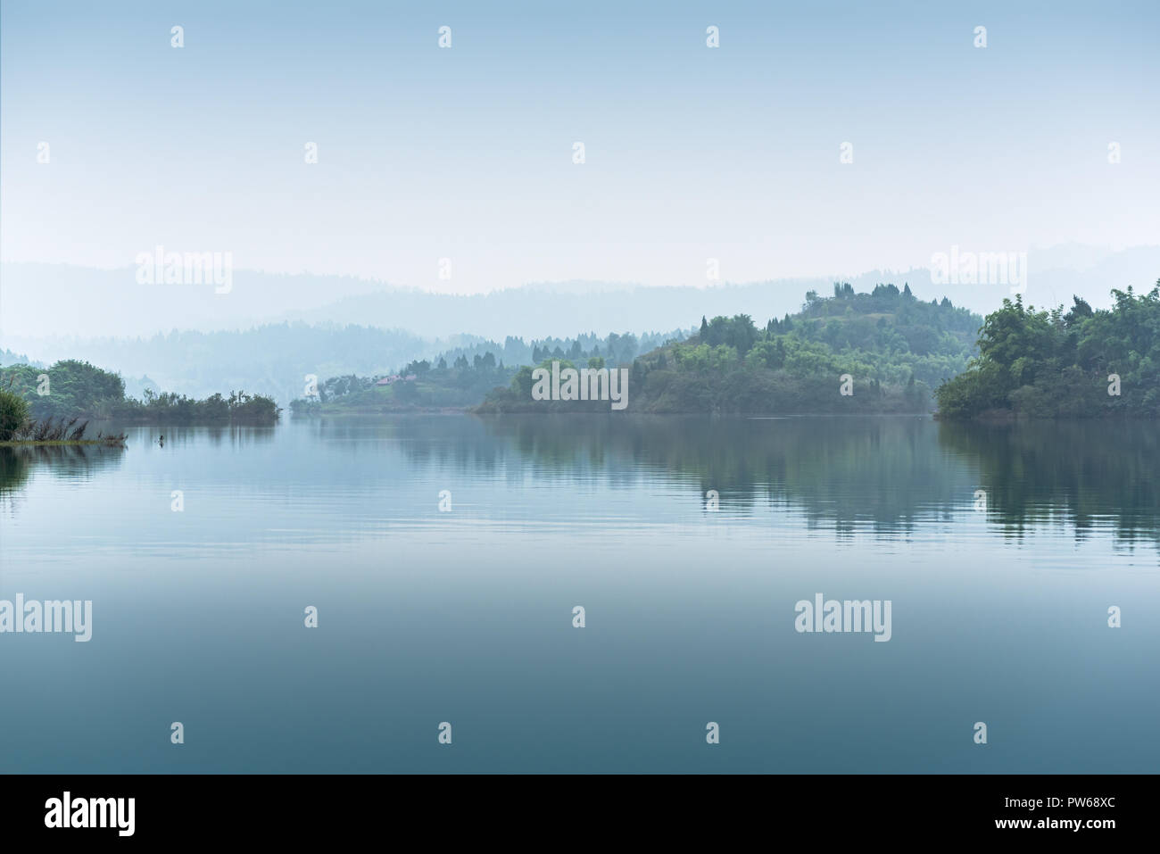 Colline con alberi nella nebbia da un lago in JingYang, nella provincia di Sichuan, in Cina Foto Stock