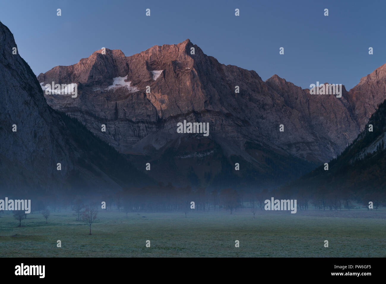 Nebbia sull'autunnale Grosser Ahornboden di fronte alle pareti rocciose dei monti Karwendel all'alba mattutina rossastra, Tirolo, Austria Foto Stock